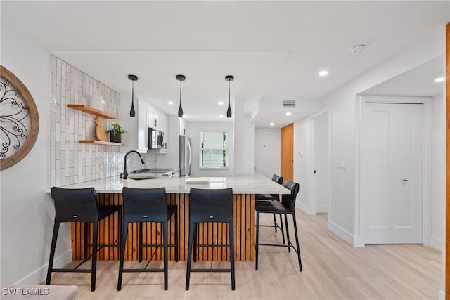 kitchen with stainless steel appliances, kitchen peninsula, a breakfast bar, pendant lighting, and white cabinetry