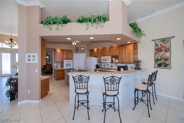 kitchen featuring a breakfast bar area, ornamental molding, light tile patterned floors, kitchen peninsula, and white appliances