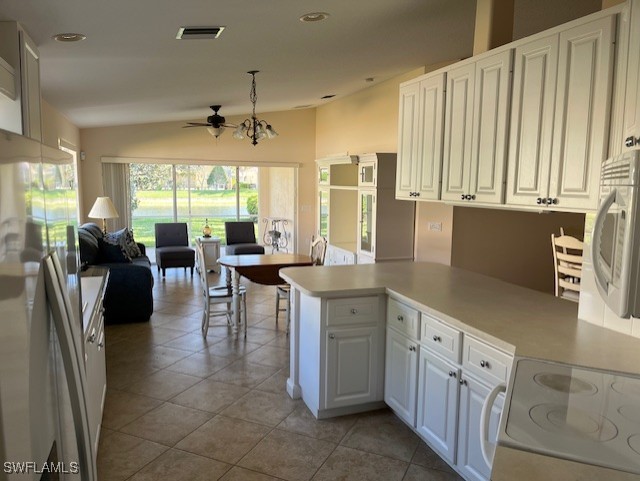 kitchen featuring ceiling fan with notable chandelier, white cabinets, hanging light fixtures, kitchen peninsula, and stove