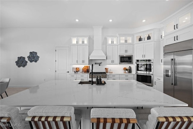 kitchen with a kitchen bar, built in appliances, light stone countertops, and custom exhaust hood