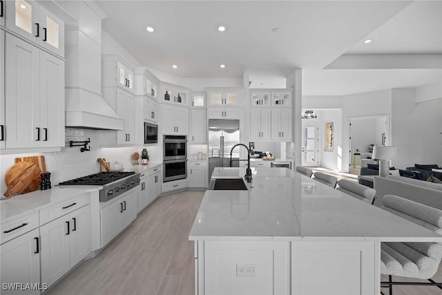 kitchen featuring a large island, sink, premium range hood, built in appliances, and a breakfast bar area