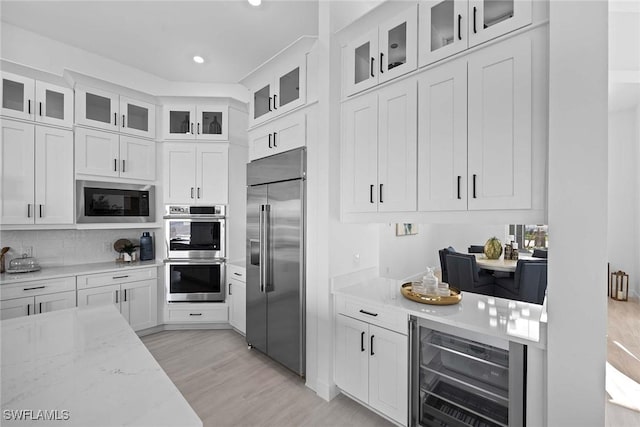 kitchen featuring built in appliances, light stone countertops, white cabinets, and beverage cooler