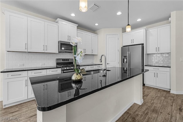 kitchen with a center island with sink, decorative light fixtures, white cabinetry, and appliances with stainless steel finishes