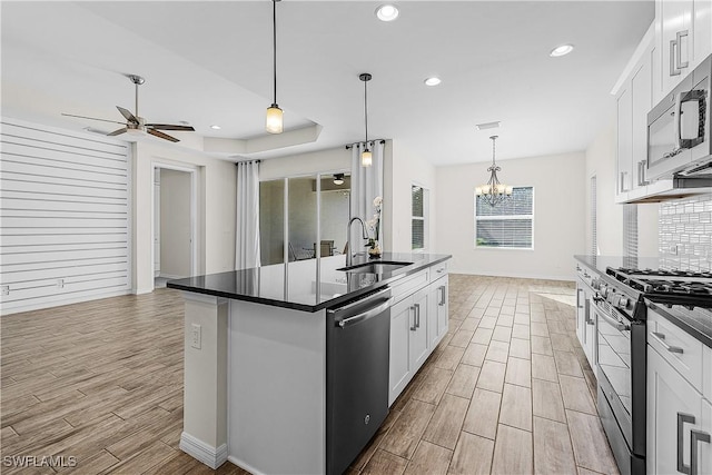 kitchen with stainless steel appliances, a center island with sink, white cabinets, and ceiling fan with notable chandelier