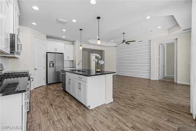 kitchen with stainless steel appliances, white cabinets, a kitchen island with sink, and hanging light fixtures