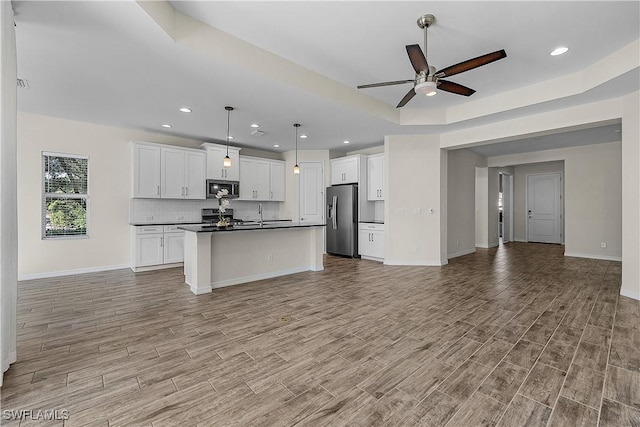 kitchen with an island with sink, appliances with stainless steel finishes, hanging light fixtures, and white cabinetry