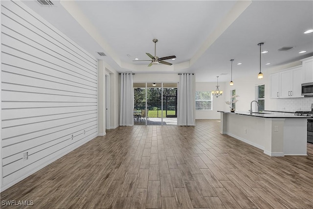 unfurnished living room with sink, ceiling fan with notable chandelier, and a tray ceiling