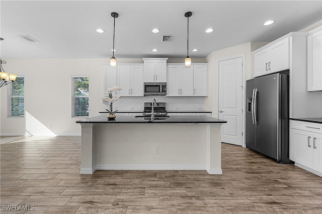 kitchen with a center island with sink, appliances with stainless steel finishes, a notable chandelier, pendant lighting, and white cabinetry