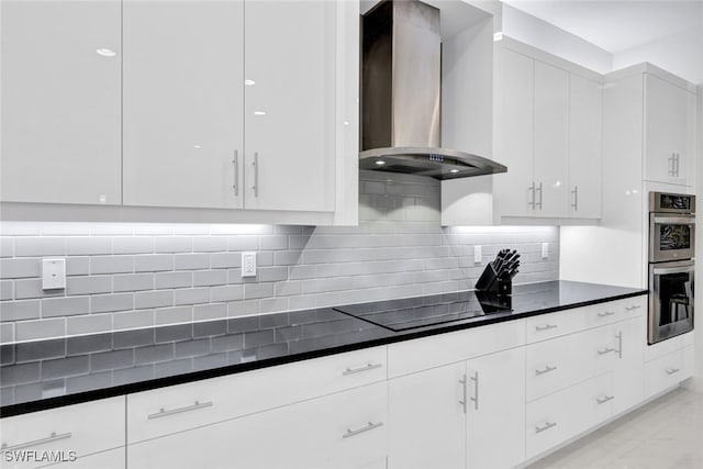 kitchen with backsplash, black electric stovetop, white cabinetry, double oven, and wall chimney exhaust hood