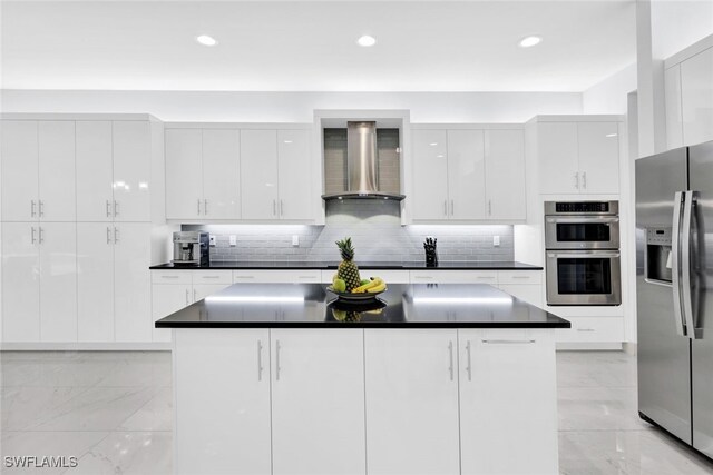 kitchen featuring white cabinets, a center island, wall chimney range hood, stainless steel appliances, and decorative backsplash