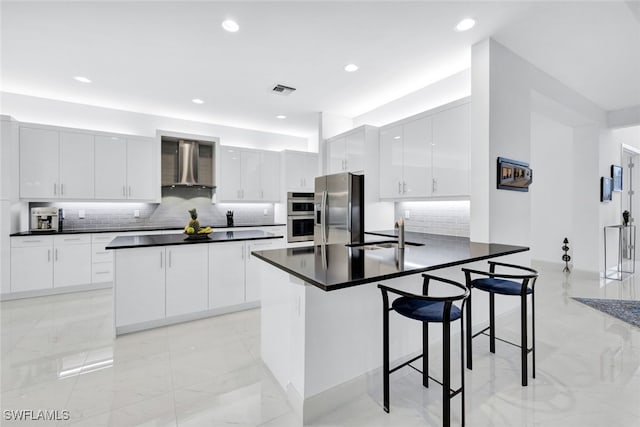 kitchen with wall chimney range hood, a breakfast bar, sink, appliances with stainless steel finishes, and white cabinets