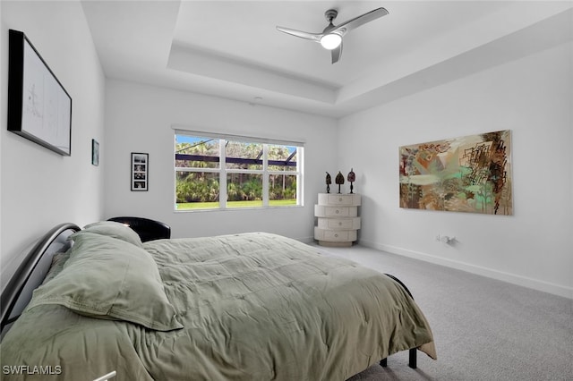 carpeted bedroom with ceiling fan and a tray ceiling