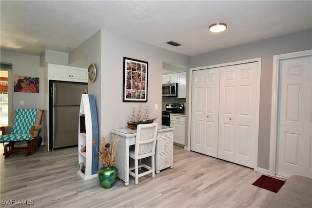 kitchen featuring white cabinets, backsplash, appliances with stainless steel finishes, and light hardwood / wood-style flooring