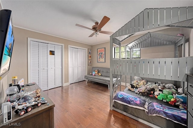 bedroom featuring ceiling fan, two closets, ornamental molding, and hardwood / wood-style floors