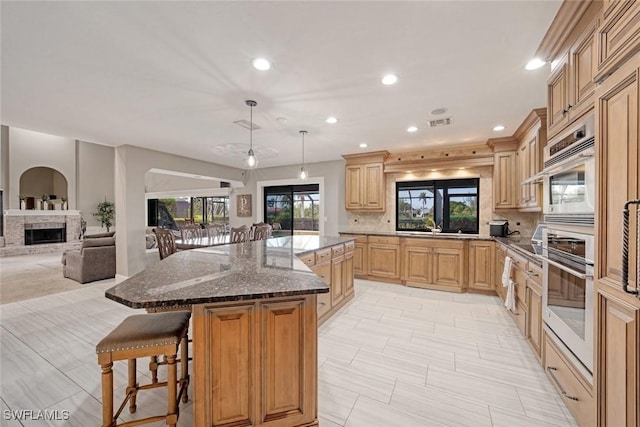 kitchen with a kitchen bar, stainless steel oven, tasteful backsplash, decorative light fixtures, and a center island