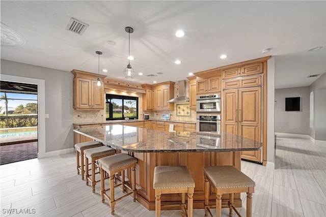 kitchen with a wealth of natural light, backsplash, wall chimney exhaust hood, and dark stone counters