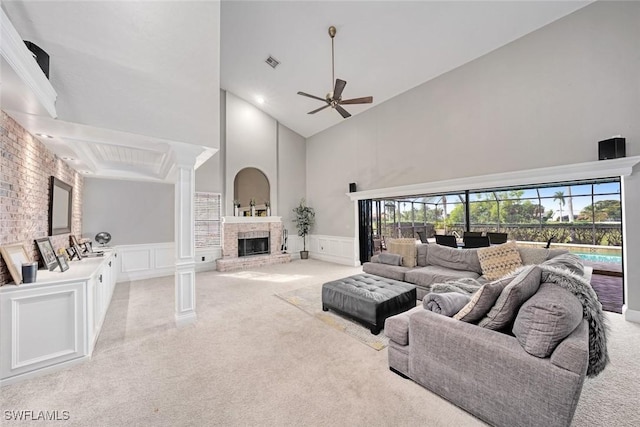 carpeted living room with ceiling fan, a fireplace, a towering ceiling, and ornate columns