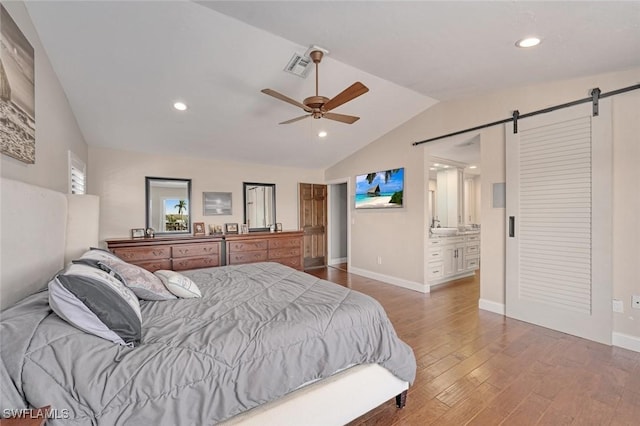 bedroom featuring ensuite bath, dark hardwood / wood-style flooring, vaulted ceiling, ceiling fan, and a barn door