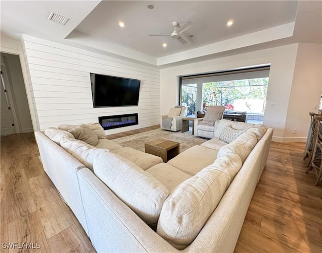 living room featuring light wood finished floors, a raised ceiling, and a glass covered fireplace