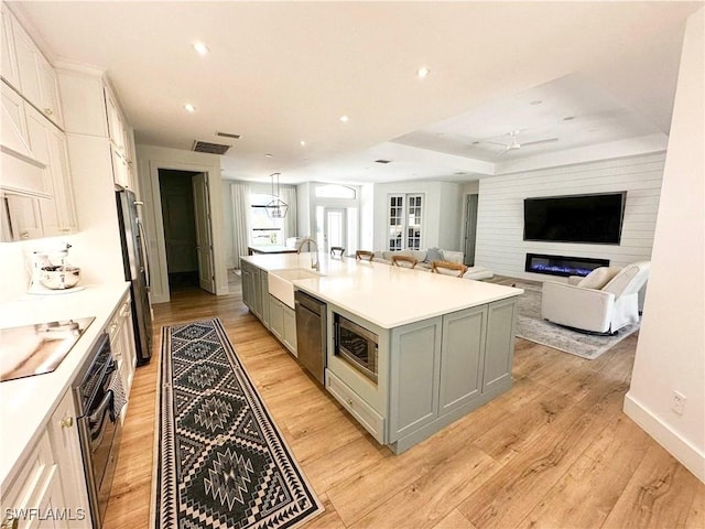 kitchen with a center island with sink, light countertops, appliances with stainless steel finishes, open floor plan, and white cabinetry