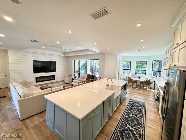 kitchen with light countertops, visible vents, open floor plan, a kitchen island with sink, and a sink