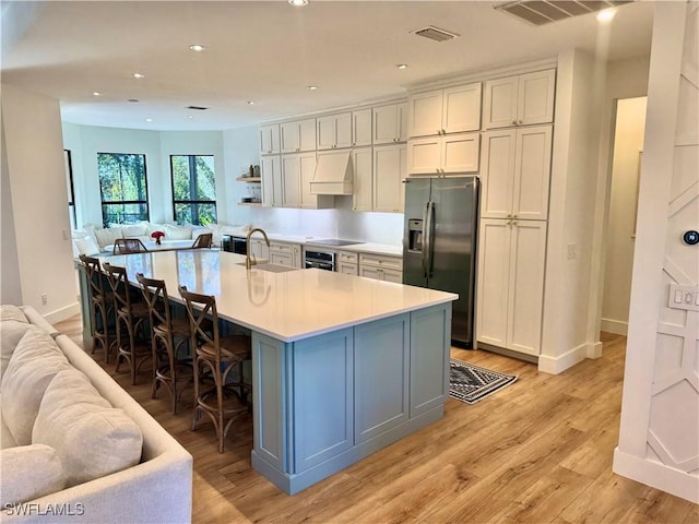 kitchen with appliances with stainless steel finishes, open floor plan, a kitchen island with sink, light countertops, and a sink