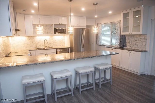 kitchen with appliances with stainless steel finishes, sink, white cabinets, kitchen peninsula, and dark wood-type flooring