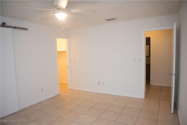 unfurnished room with ceiling fan, a barn door, and light tile patterned flooring