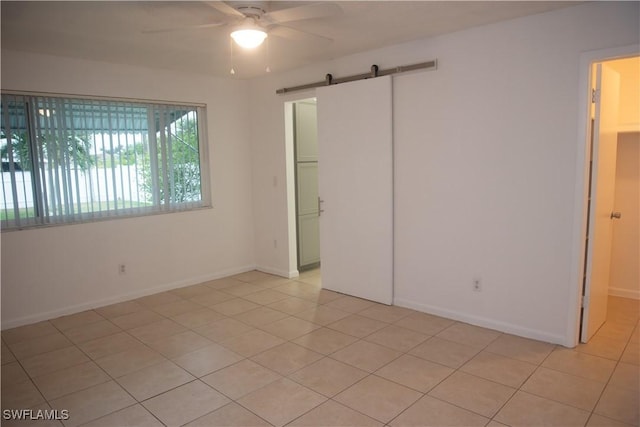 unfurnished bedroom featuring a closet, light tile patterned floors, ceiling fan, and a barn door