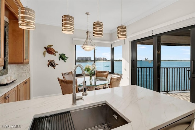 kitchen with backsplash, a water view, sink, light stone countertops, and decorative light fixtures