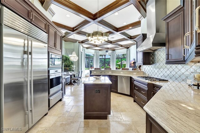 kitchen featuring kitchen peninsula, coffered ceiling, ventilation hood, decorative light fixtures, and built in appliances