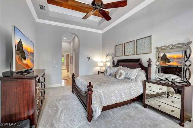 bedroom with ceiling fan, ensuite bathroom, a raised ceiling, crown molding, and light carpet