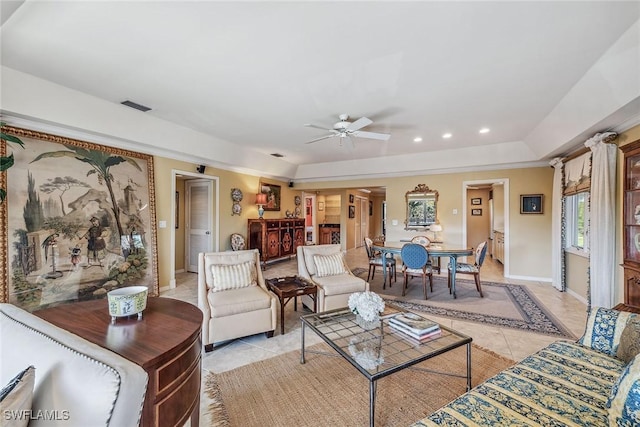 living room with a tray ceiling, ceiling fan, and light tile patterned flooring