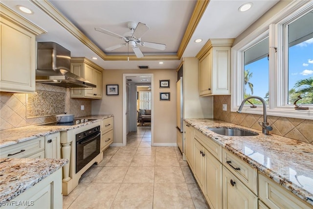 kitchen featuring wall chimney exhaust hood, a raised ceiling, sink, black appliances, and cream cabinetry