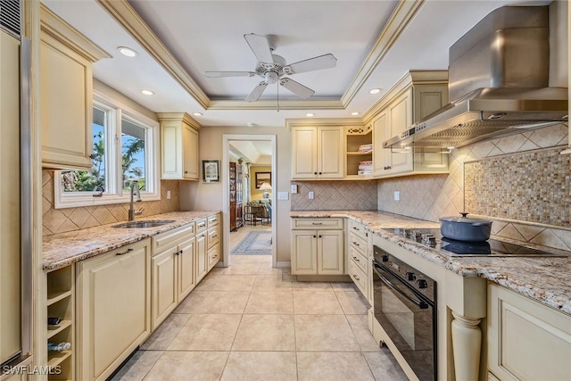 kitchen featuring cream cabinets, black appliances, sink, wall chimney exhaust hood, and a tray ceiling