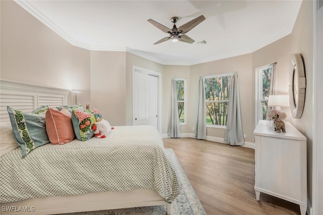 bedroom featuring ceiling fan, light hardwood / wood-style floors, ornamental molding, and a closet