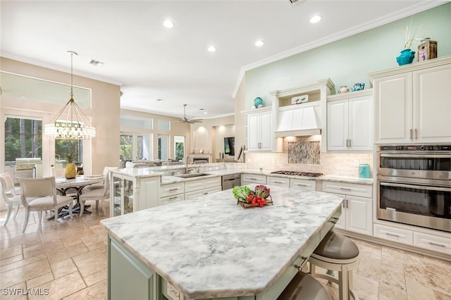 kitchen with custom exhaust hood, hanging light fixtures, appliances with stainless steel finishes, a kitchen island, and kitchen peninsula