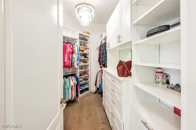 spacious closet with light hardwood / wood-style floors and a notable chandelier