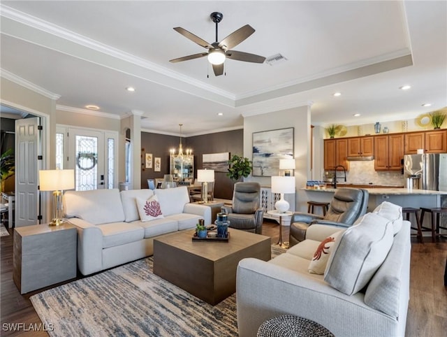 living room with ornamental molding, ceiling fan with notable chandelier, dark hardwood / wood-style flooring, and a tray ceiling