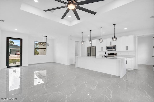 kitchen with white cabinetry, hanging light fixtures, a raised ceiling, stainless steel appliances, and a kitchen island with sink