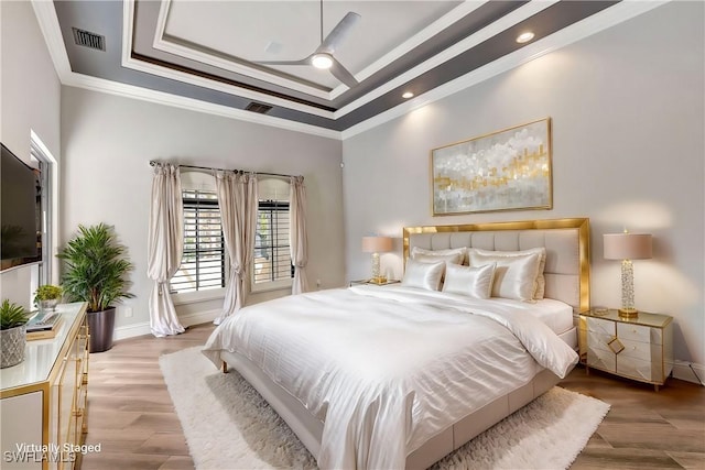 bedroom featuring ceiling fan, ornamental molding, a tray ceiling, and light hardwood / wood-style flooring