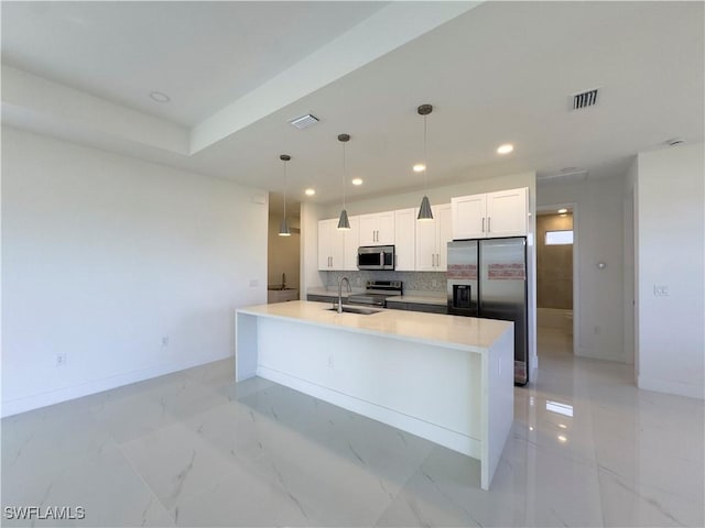 kitchen featuring appliances with stainless steel finishes, an island with sink, white cabinets, decorative light fixtures, and sink