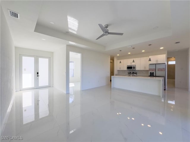 unfurnished living room featuring french doors, ceiling fan, and a tray ceiling