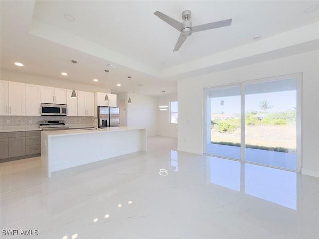 kitchen featuring stainless steel appliances, ceiling fan, a tray ceiling, white cabinets, and tasteful backsplash