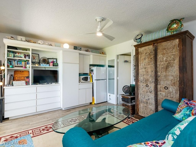 living room with ceiling fan, light wood-type flooring, and a textured ceiling