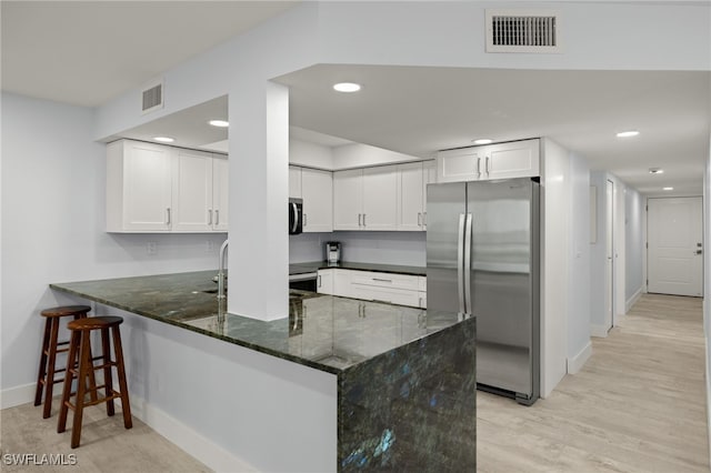 kitchen with white cabinets, stainless steel appliances, dark stone countertops, kitchen peninsula, and light wood-type flooring