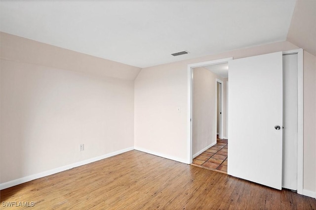 spare room with lofted ceiling, wood finished floors, visible vents, and baseboards