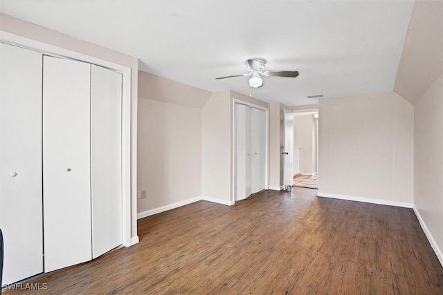 unfurnished bedroom featuring a ceiling fan, wood finished floors, baseboards, vaulted ceiling, and multiple closets