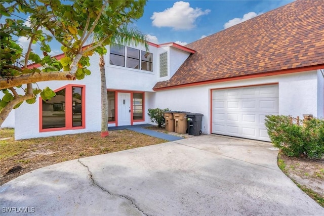 view of front facade featuring concrete driveway, an attached garage, roof with shingles, and stucco siding