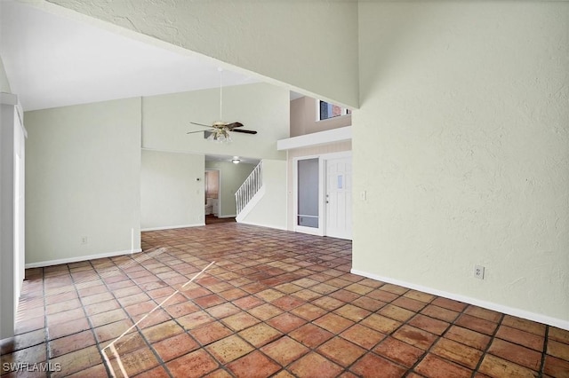 tiled empty room with high vaulted ceiling, a ceiling fan, stairway, baseboards, and a textured wall